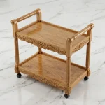 Hand carved Sheesham wood tea trolley with two shelves and flower carvings on white marble floor by Haq Bahoo Furniture