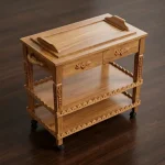 Sheesham wood tea trolley with two drawers, removable top tray, carved wavy edge rails, and black wheels on wooden floor by Haq Bahoo Furniture Chiniot