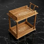 Handcrafted modern bar cart with light walnut finish, carved borders, inlay detailing, two tiers, and caster wheels.